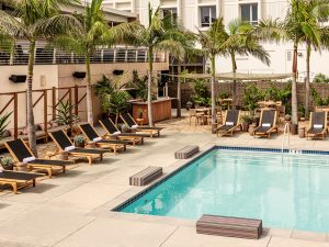 Pool area with chaise lounge chairs, pam trees and Hotel June in the background