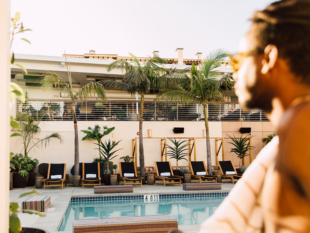 Pool with cushions next to edge, lounge chairs in the background and shirtless man in the foreground