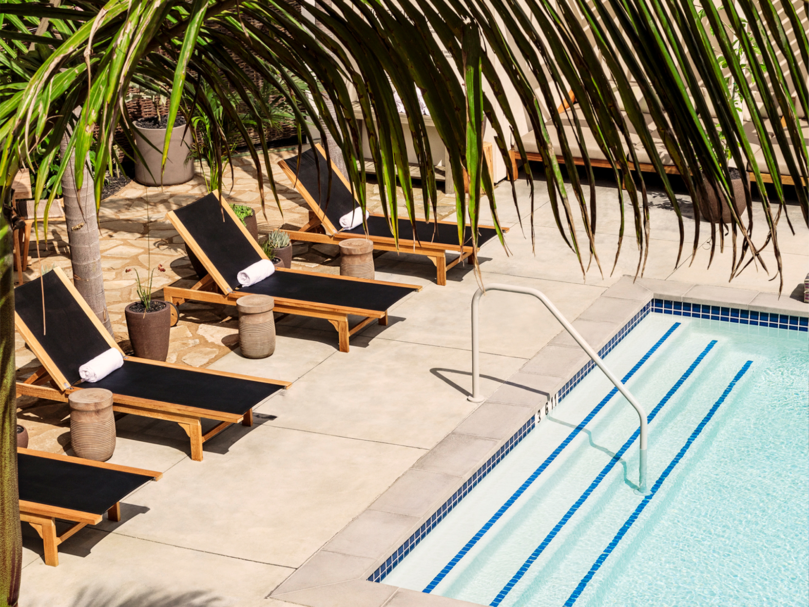 Overhead view of pool, lounge chairs and palm leaves in the foreground